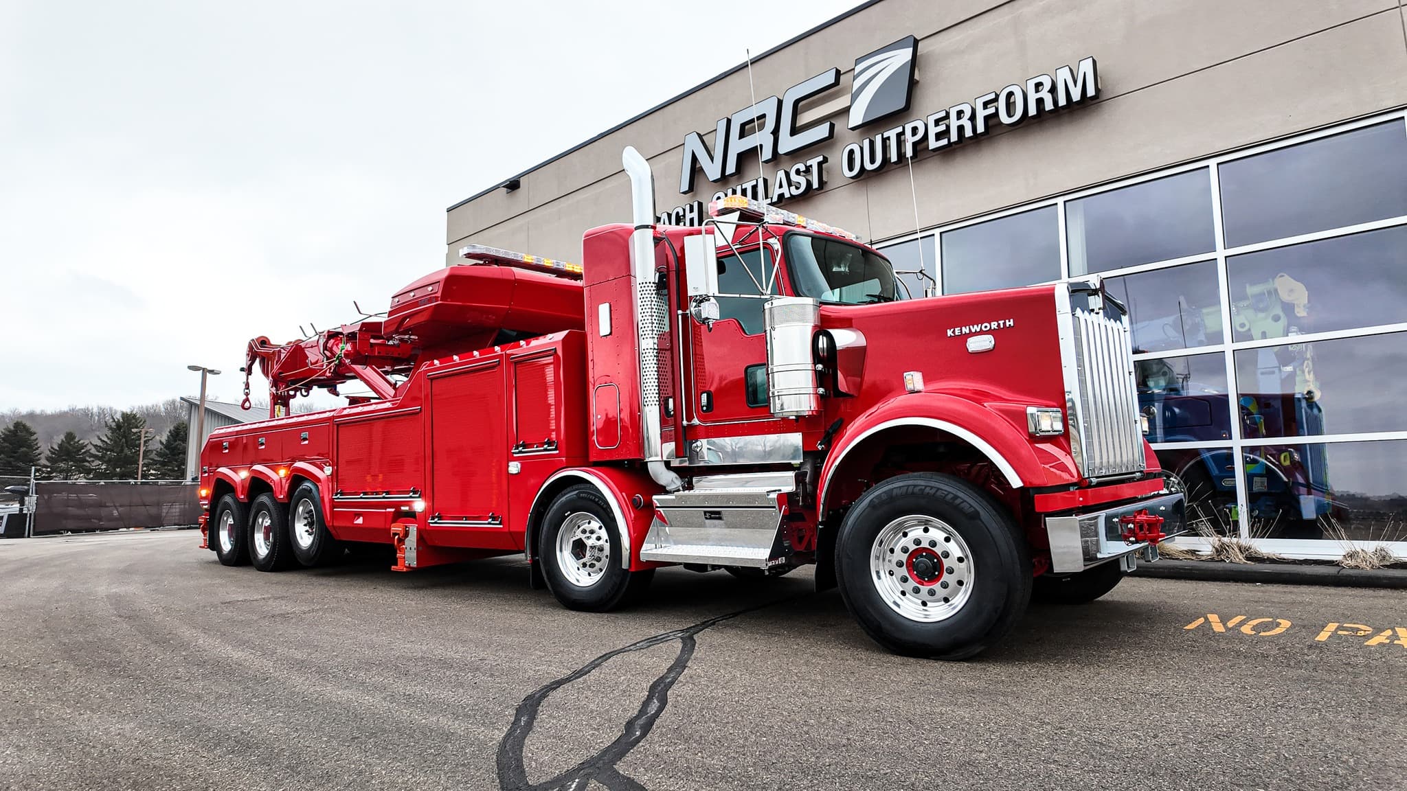 Red Kenworth NRC heavy-duty wrecker with boom and outriggers at an NRC facility